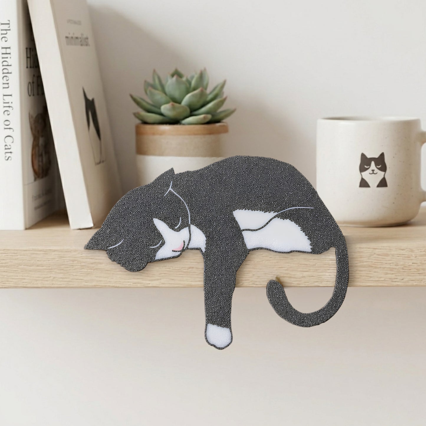 Gray and white tuxedo cat shelf pet napping on a light wood shelf beside books and a cat mug