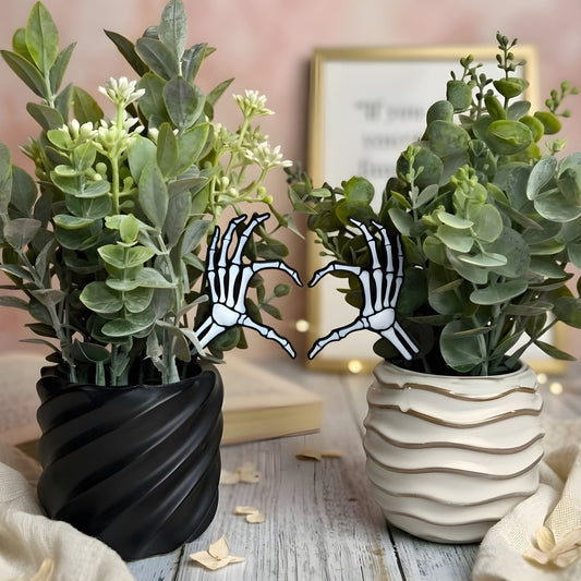 Two potted plants with skeleton hand plant stakes in front of a whimsical blurred background.