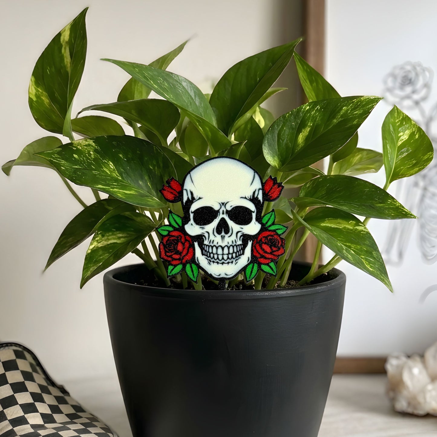 Potted plant with a decorative skull and roses plant stake in a neutral room