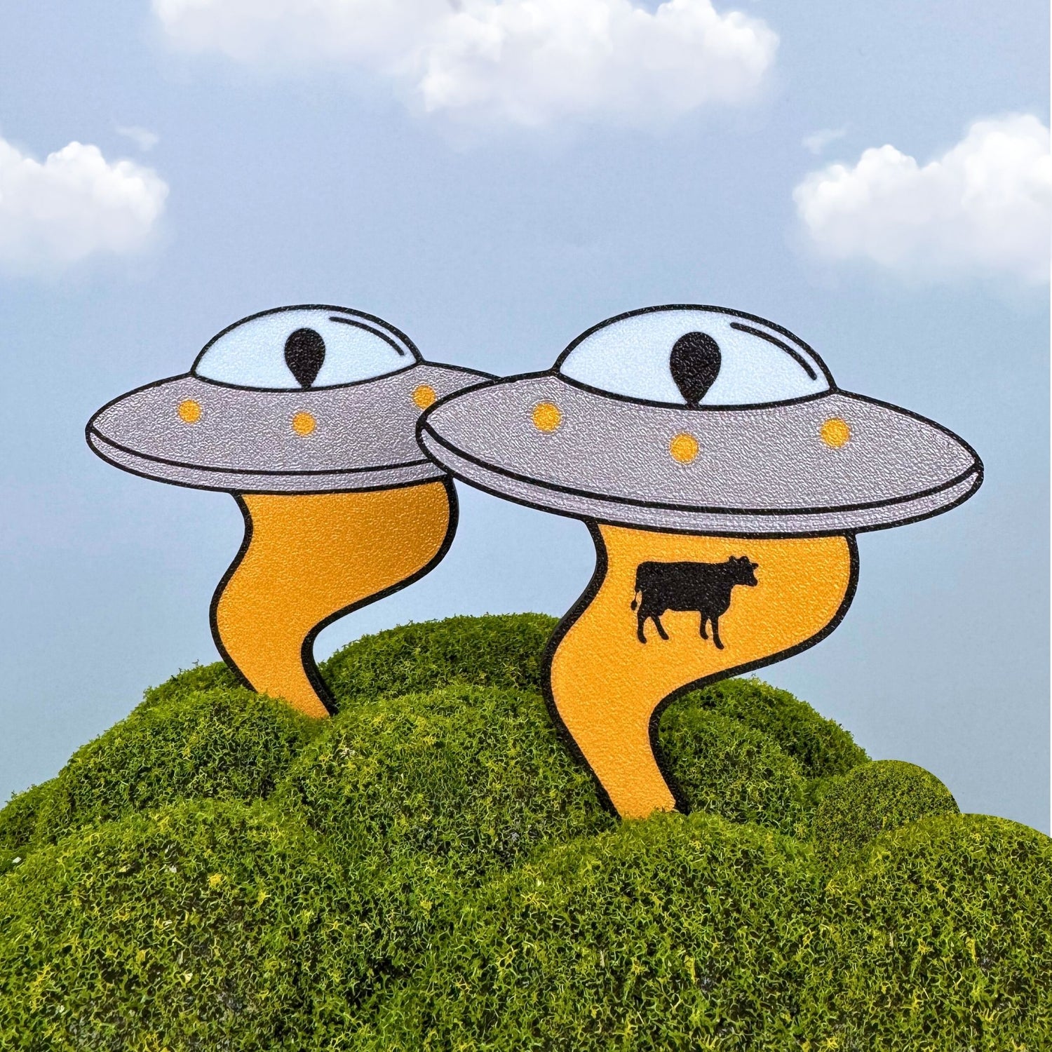 Funny UFO plant stakes with and without a cow being beamed up in a green field
