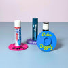 Three vibrant color combinations of the vinyl record lip balm holders including cyan blue, magenta pink, and purple