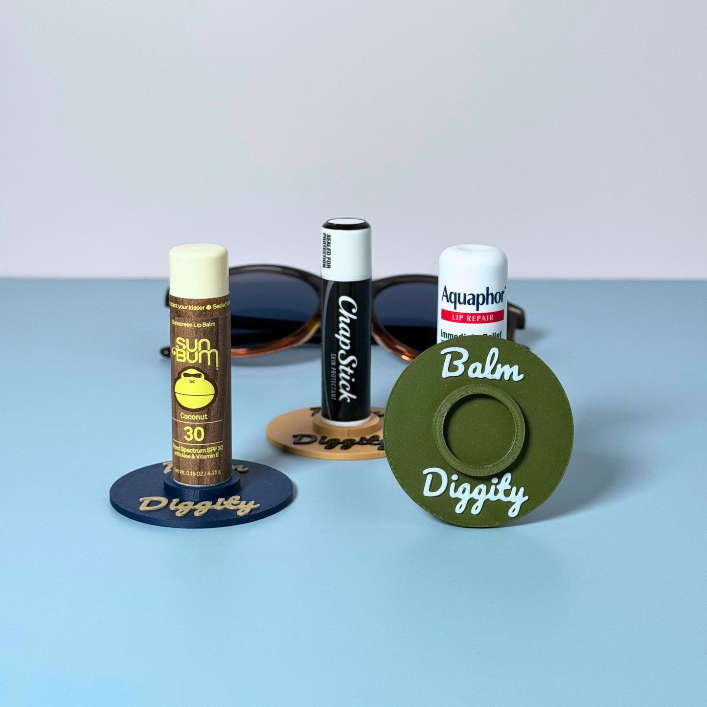 Three color combinations of the vinyl record lip balm holders including olive, beige, and navy blue