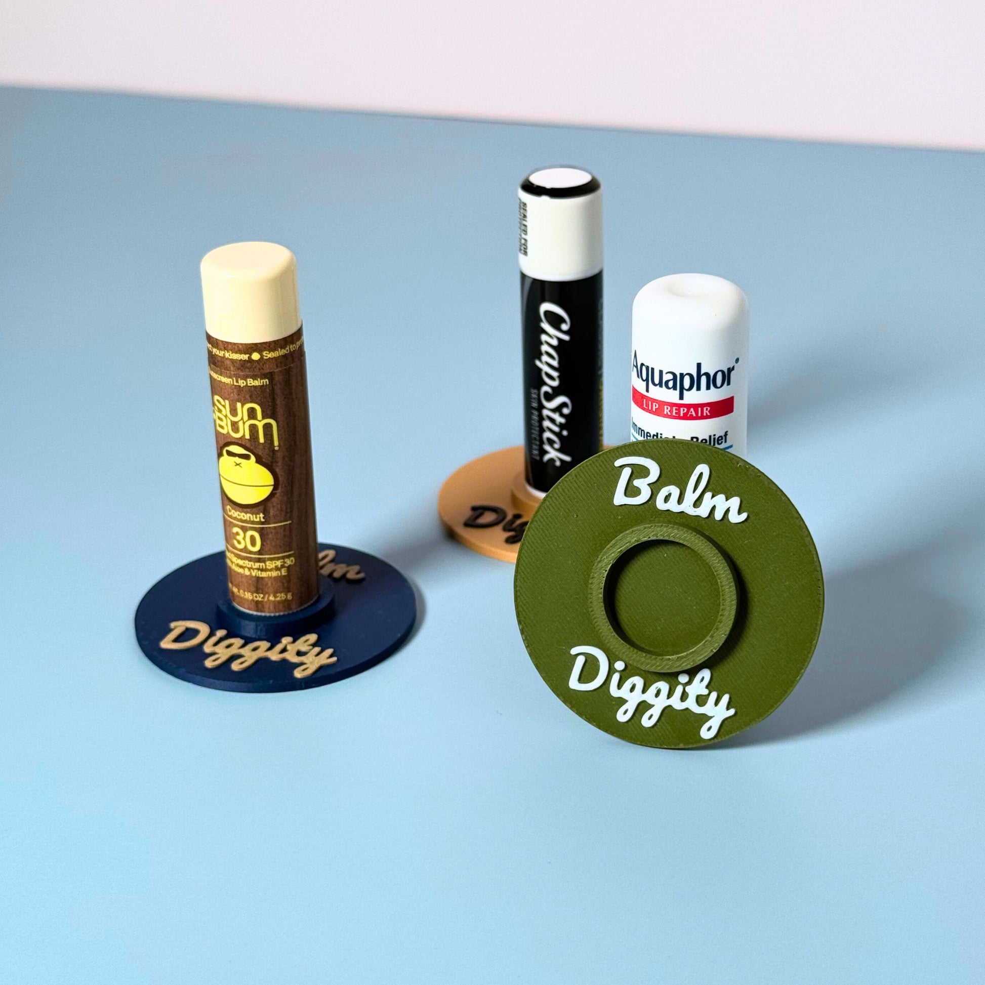 Three color combinations of the vinyl record lip balm holders including olive, beige, and navy blue