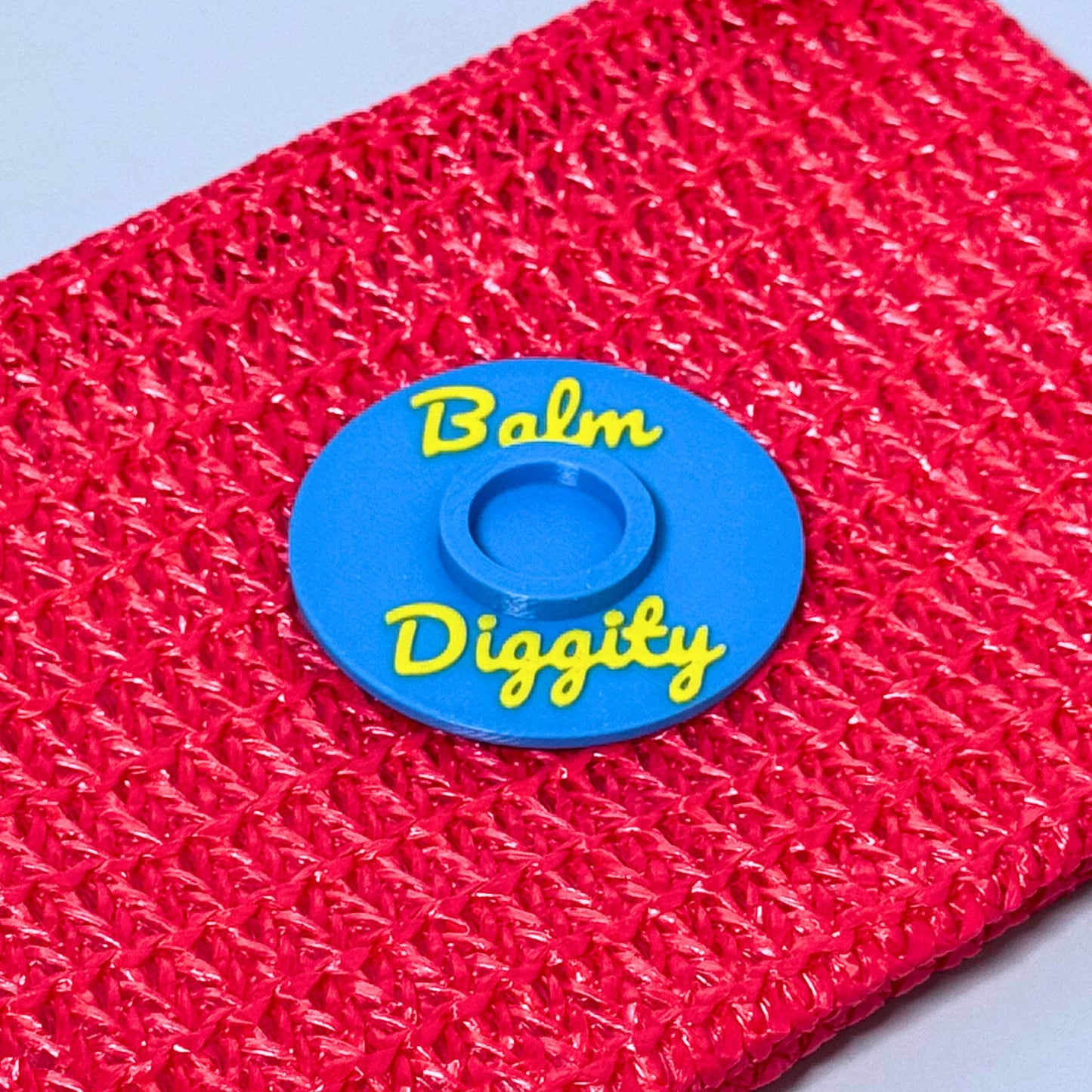A vibrant color combination of the vinyl record lip balm holders in cyan blue with yellow writing saying Balm Diggity on a bright pink pouch