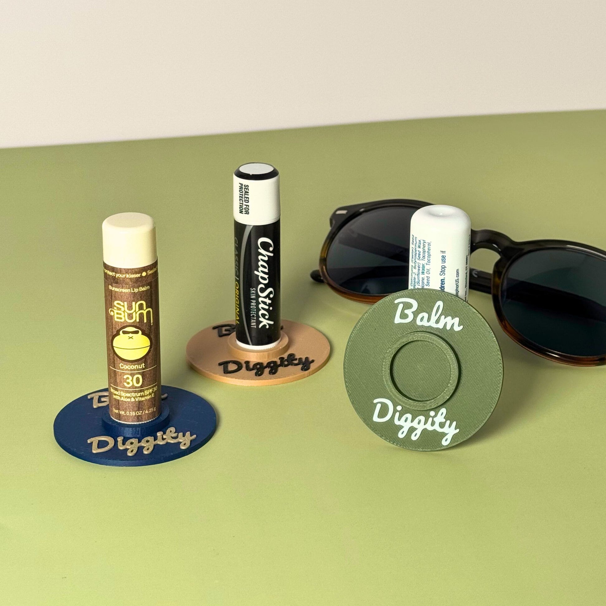 Three color combinations of the vinyl record lip balm holders including olive, beige, and navy blue