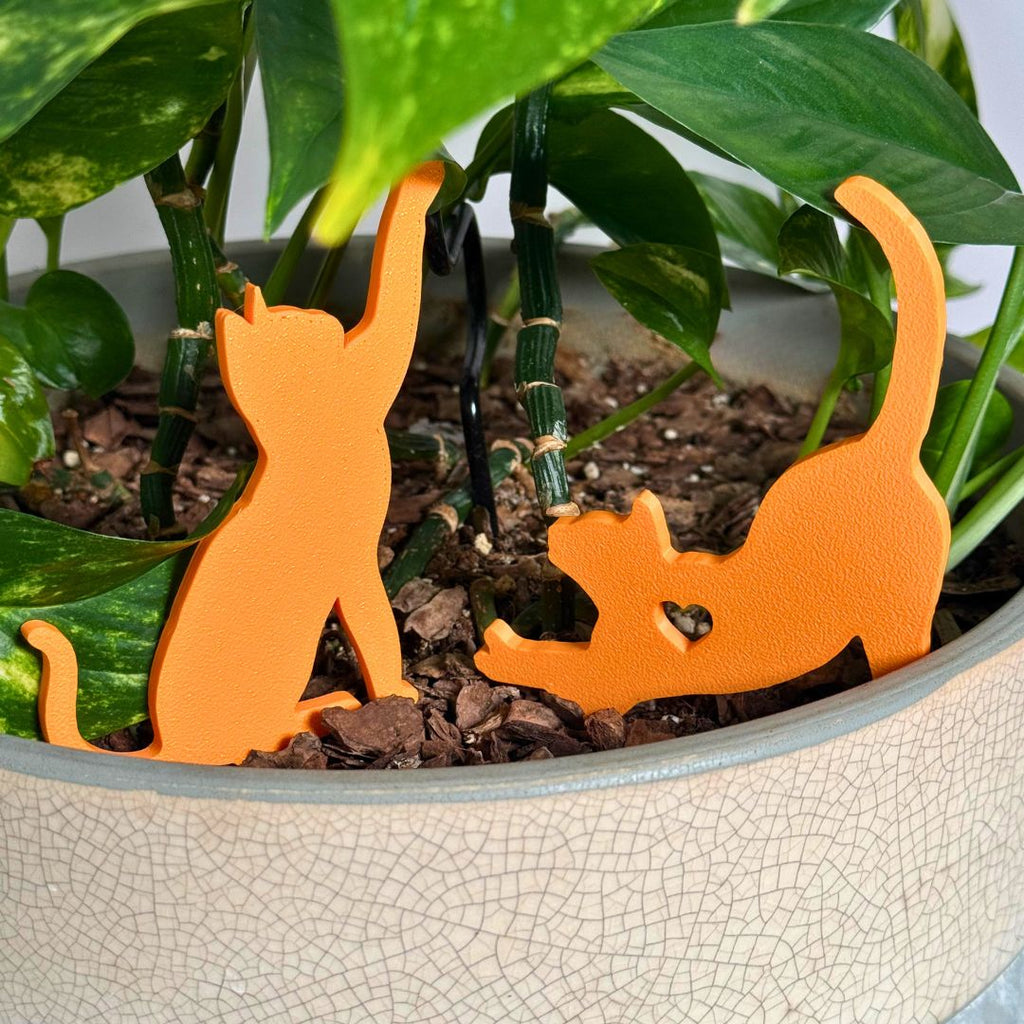 Cute set of orange cat plant stakes stretching and playing inside a houseplant