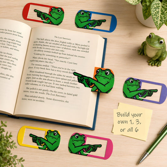 Frog bookmark clips in six colors on a desk with a book and a build your own 1, 3, or all 6 note