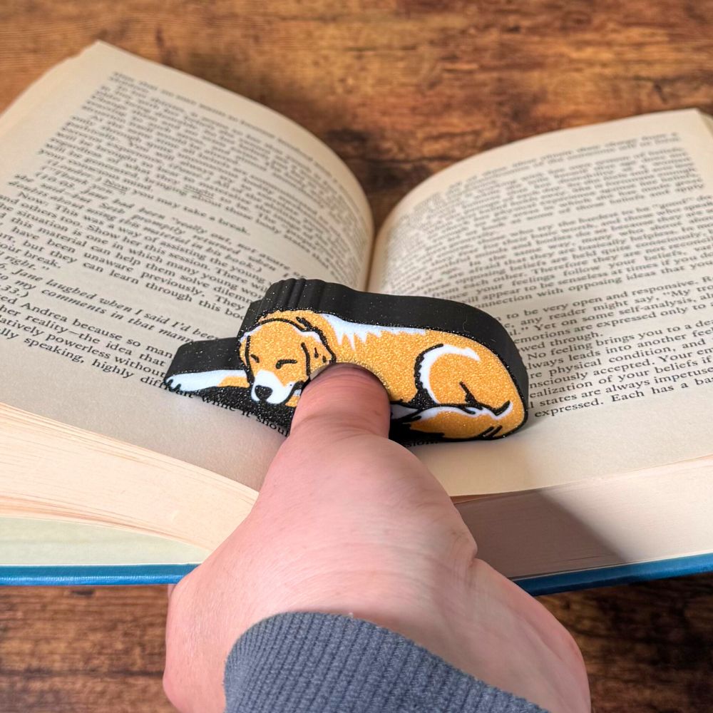 Adorable sleeping gold and white fur golden retriever dog book page holder shown holding a book open from the front view