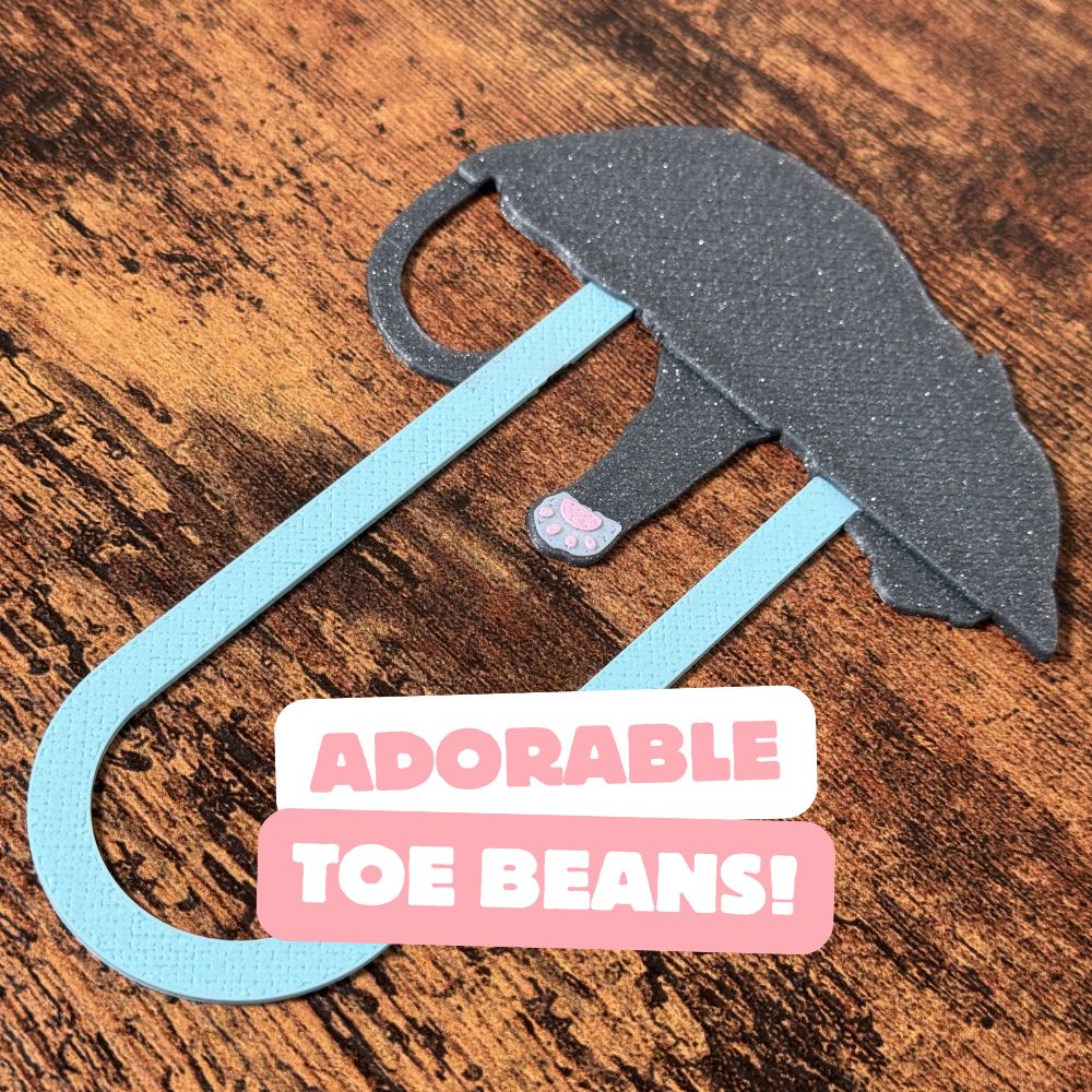 The back of a grey tuxedo cat bookmark showing the adorable pink toe beans on the back of its paw