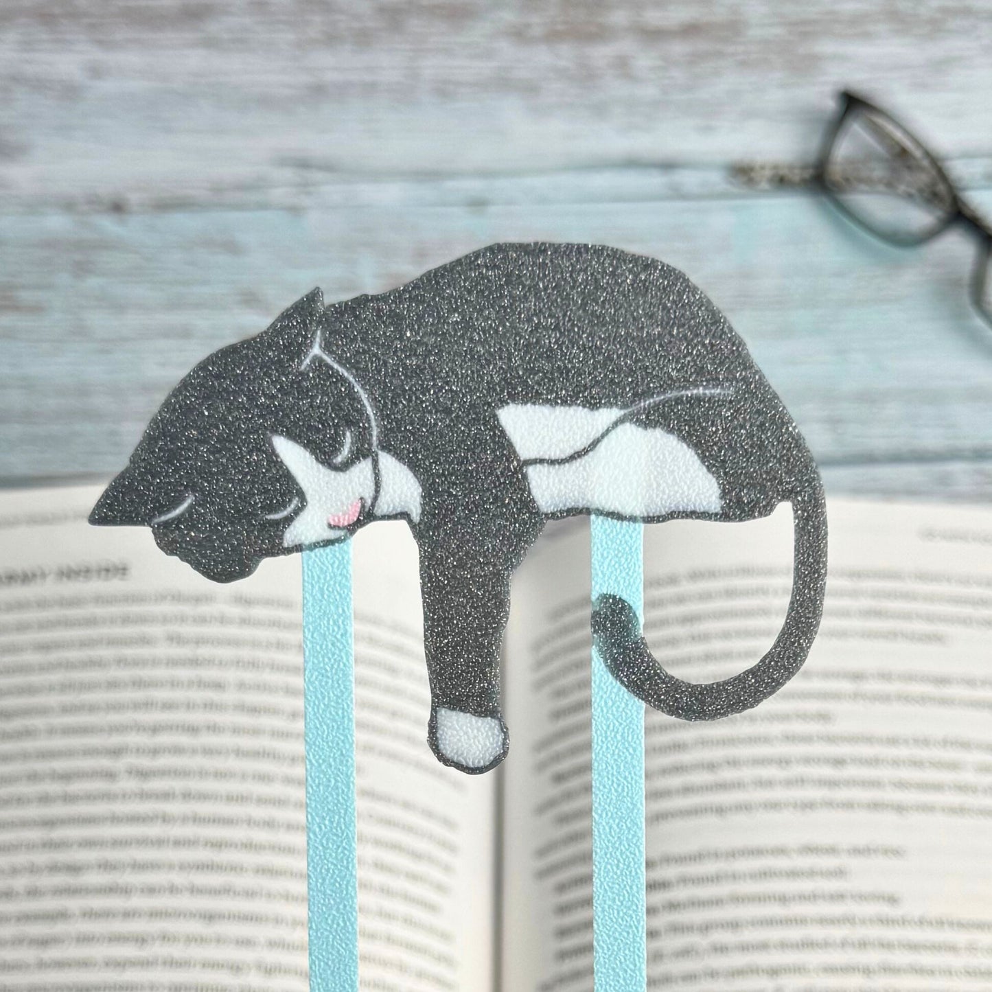 Women holding up a gray and white tuxedo cat bookmarks above a book