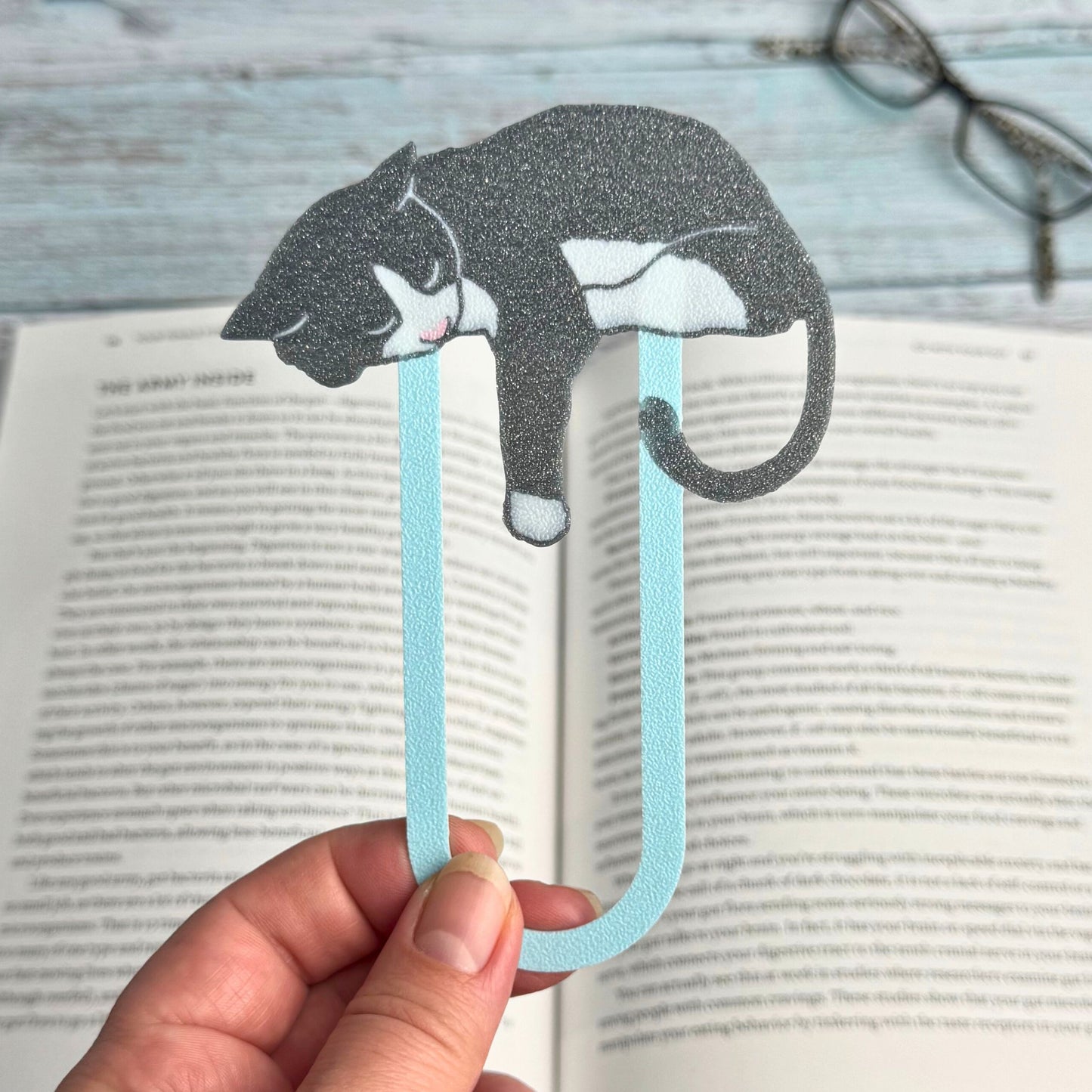Women holding up a gray and white tuxedo cat bookmarks above a book