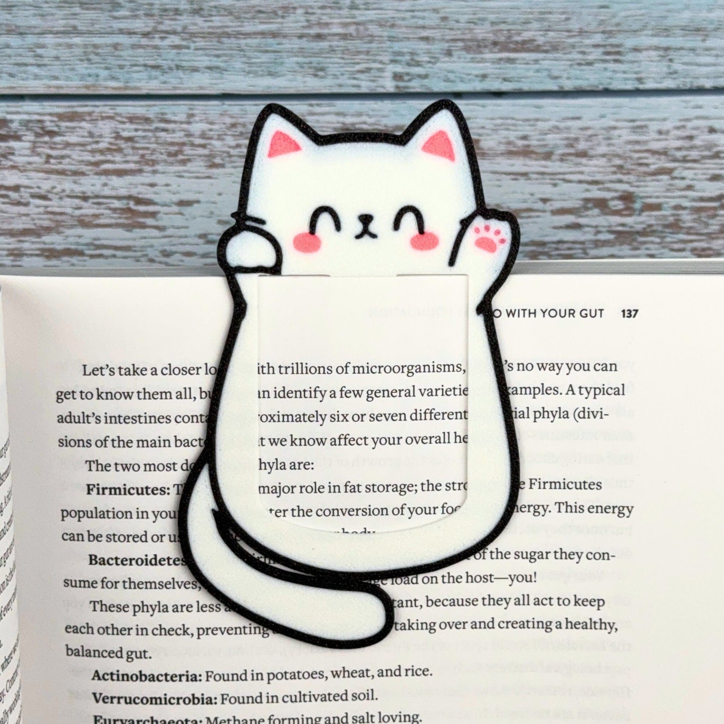 Cute kawaii style cat bookmark waving hello clipped onto the page of a book showing off its cute pink toe beans