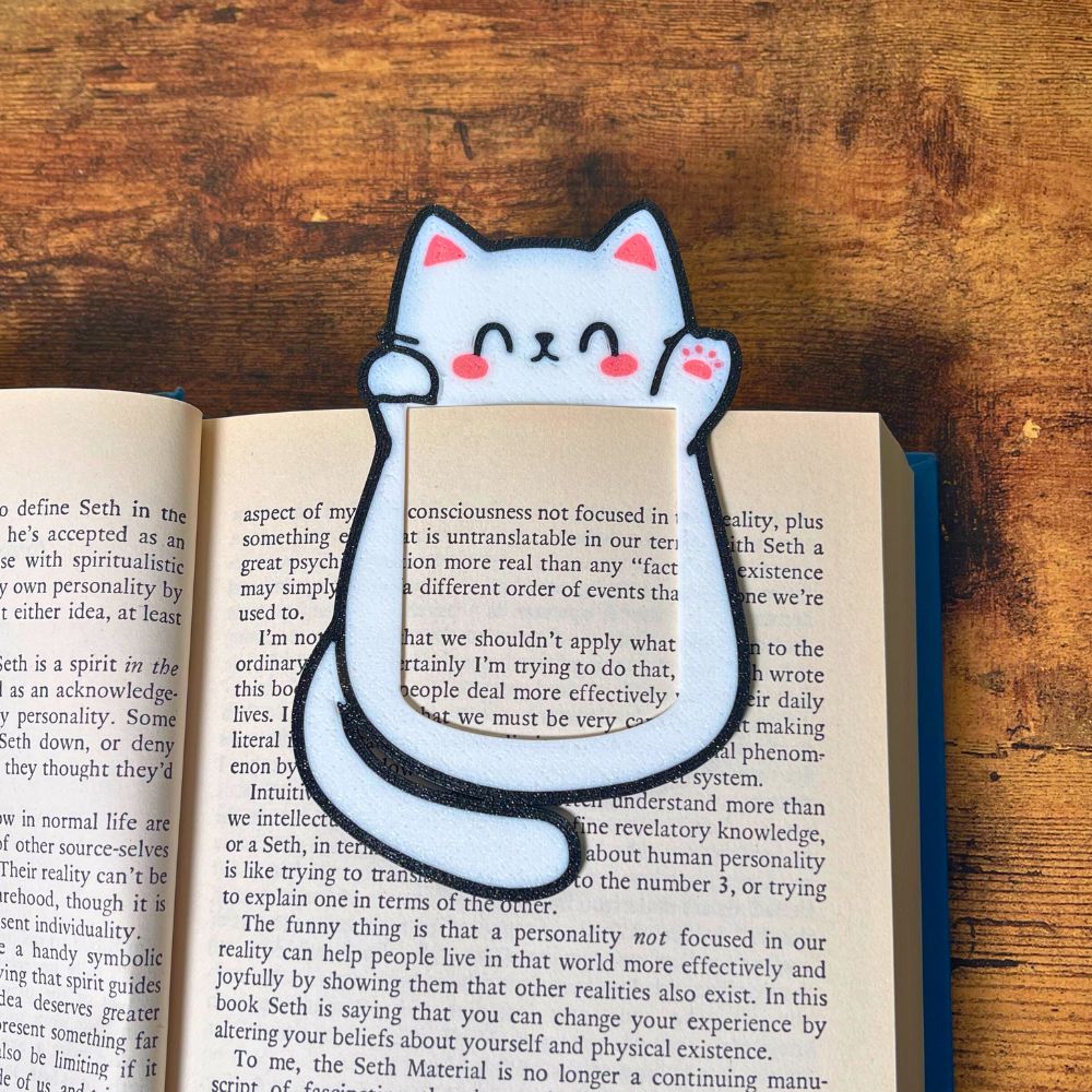 Cute kawaii style cat bookmark waving hello clipped onto the page of a blue book showing off its cute pink toe beans