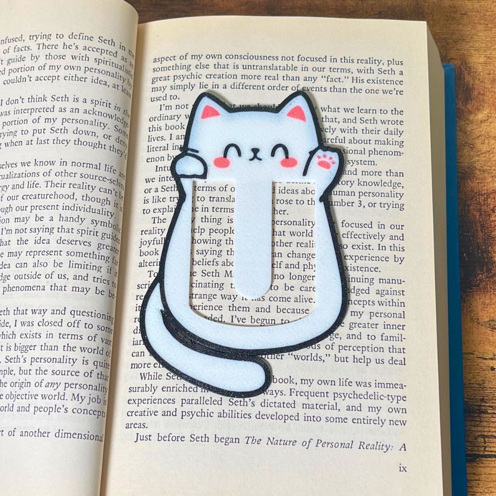 Cute kawaii style cat bookmark waving hello from inside a blue book showing off its cute pink toe beans
