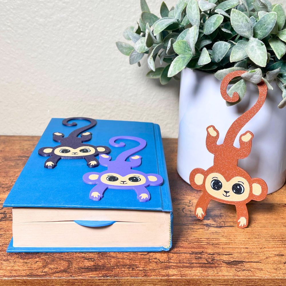 Four colors of fun monkey bookmarks hanging from a book and inside of the book