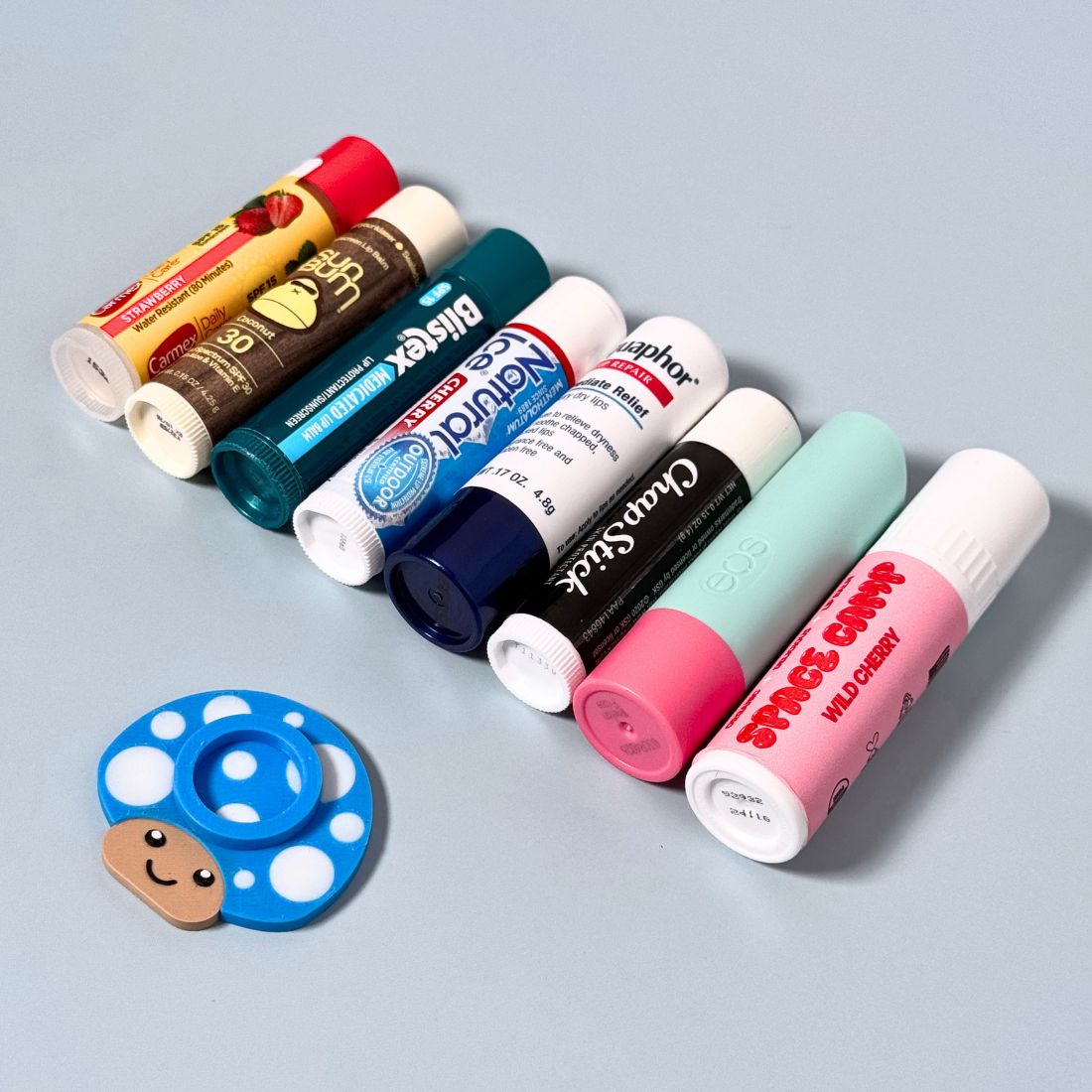 Happy little mushroom lip balm holder in cyan blue with a row of lip balms that we can fit the product size to