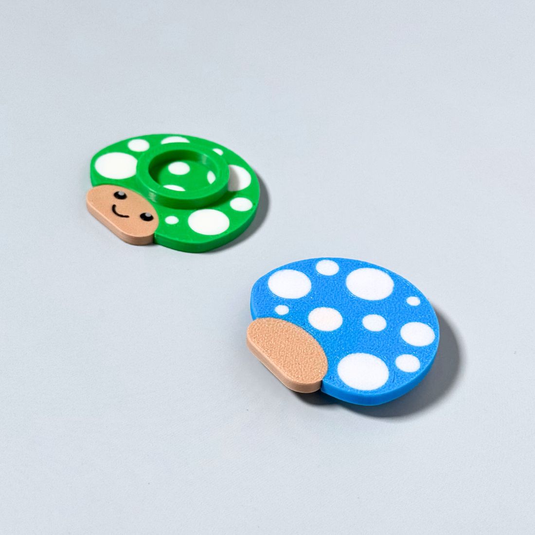 Happy little mushroom lip balm holders in cyan blue and green showing the top and bottom of the product