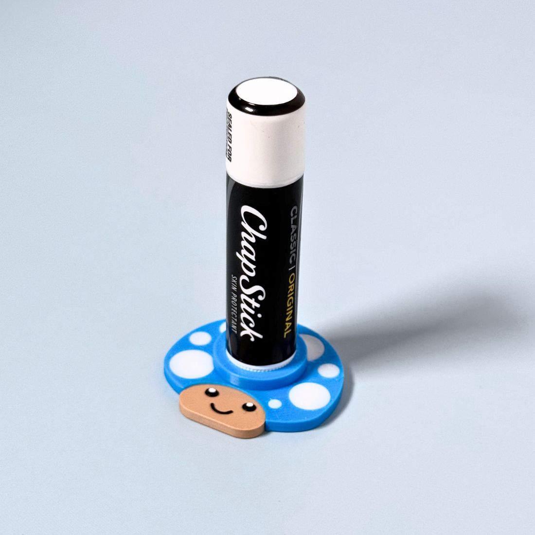 Happy little mushroom lip balm holder in cyan blue holding a chapstick up