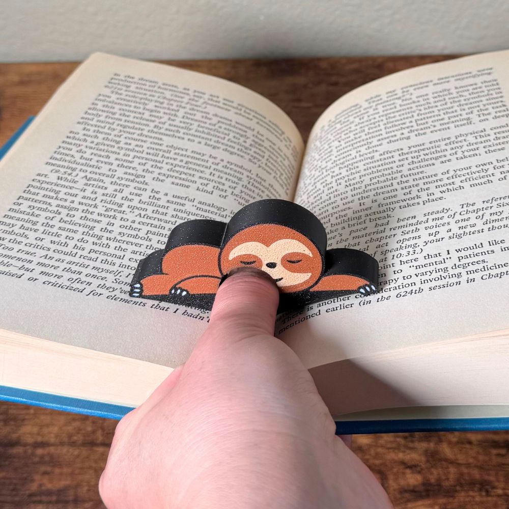 Adorable sleeping sloth book page holder shown in use holding a book open