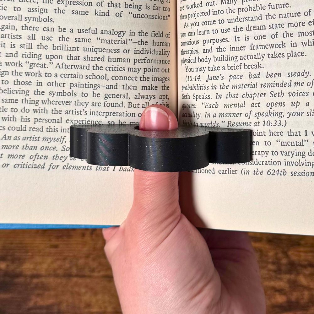 Adorable sleeping sloth book page holder shown in use holding a book open from a top view