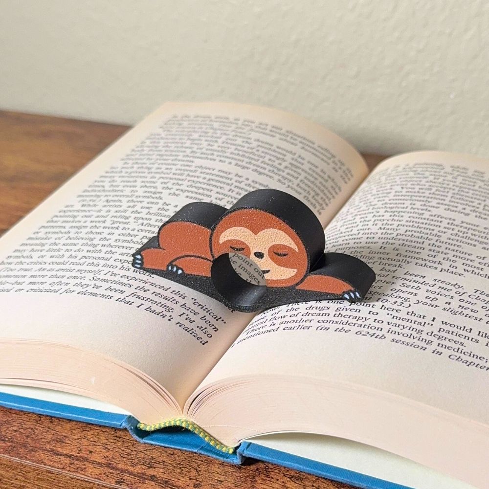 Adorable sleeping sloth book page holder shown holding a book open from a side angle