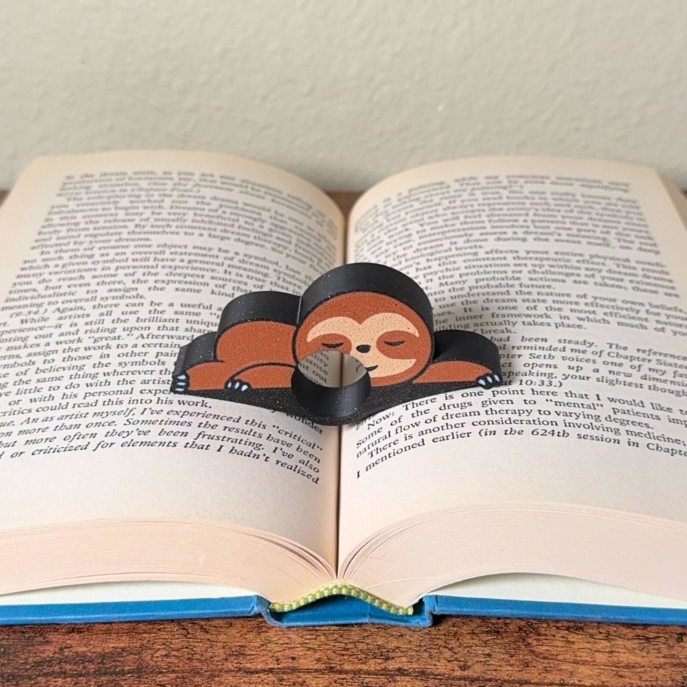 Adorable sleeping sloth book page holder shown holding a book open