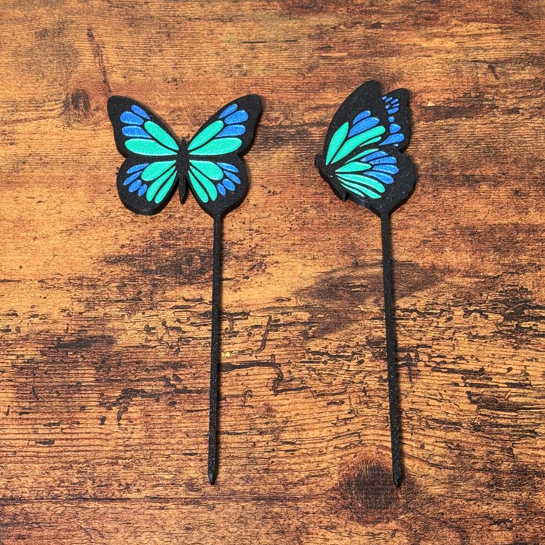 A set of 2 unique and tall butterfly plant stakes with black outlines and sparkling green and blue highlights