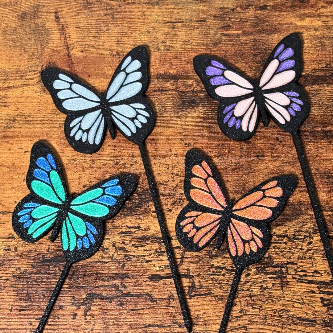 4 color combinations of the butterfly plant stakes laying on a wooden surface