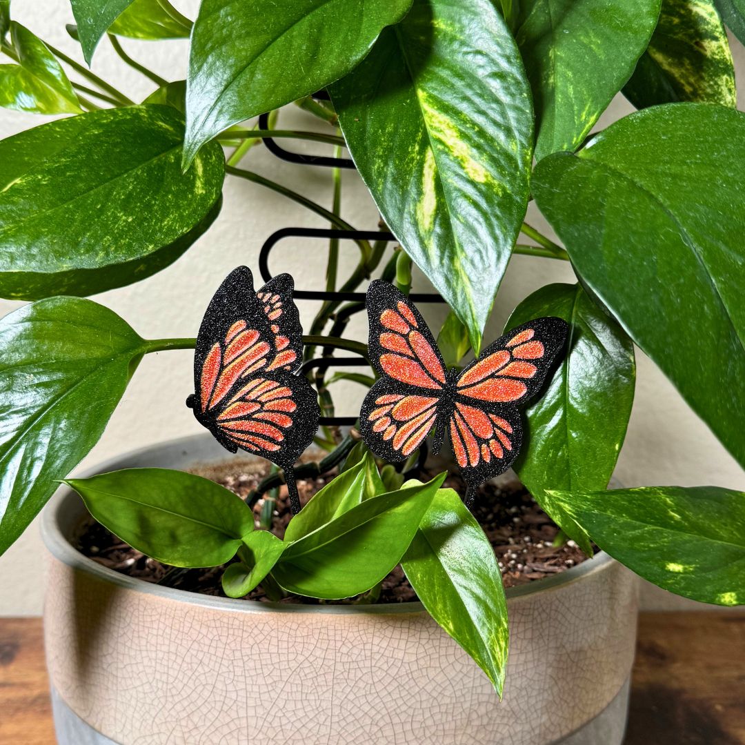 A set of 2 unique and tall butterfly plant stakes with black outlines and sparkling orange highlights