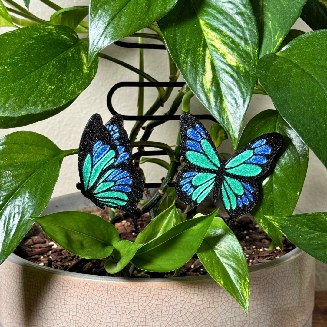 A set of 2 unique and tall butterfly plant stakes with black outlines and sparkling green and blue highlights