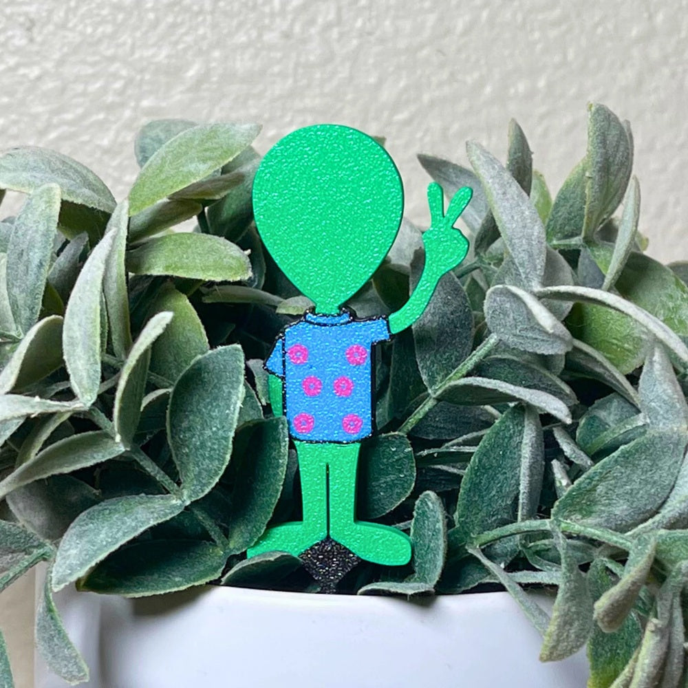 Fun alien plant stake in a Hawaiian t-shirt holding a peace sign in a houseplant showing the back of the stake