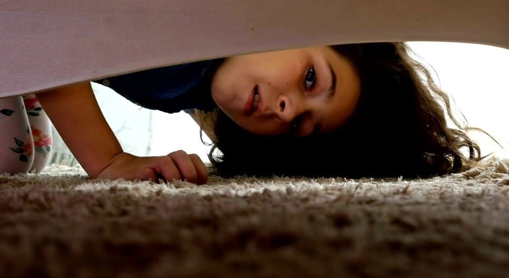 Child peeking under a bed searching the carpet, the classic hunt for a lost lip balm