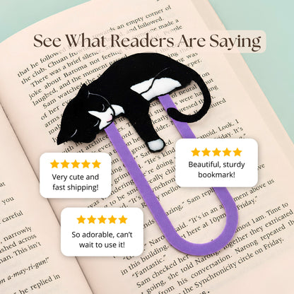 A black and white cat-shaped bookmark with purple clip placed on an open book. The image includes promotional text reading 'See What Readers Are Saying' and three review bubbles with 5 star ratings and customer feedback.