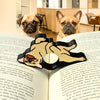 Adorable tan bulldog page holder resting across an open book with two curious pug and French bulldog dogs in the background, showcasing a cute and functional reading accessory for book lovers.