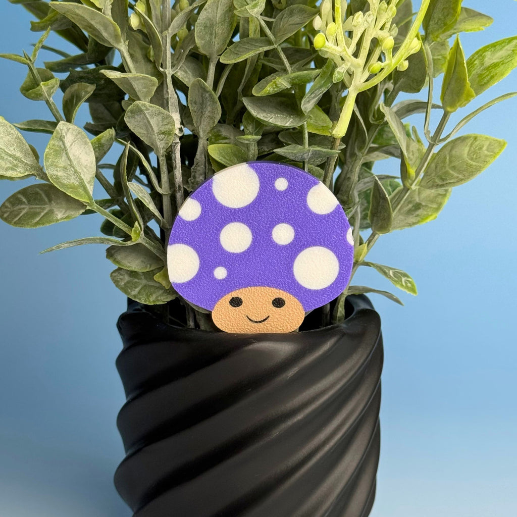 Purple mushroom plant stake with a happy face rising from a leafy plant in a black planter