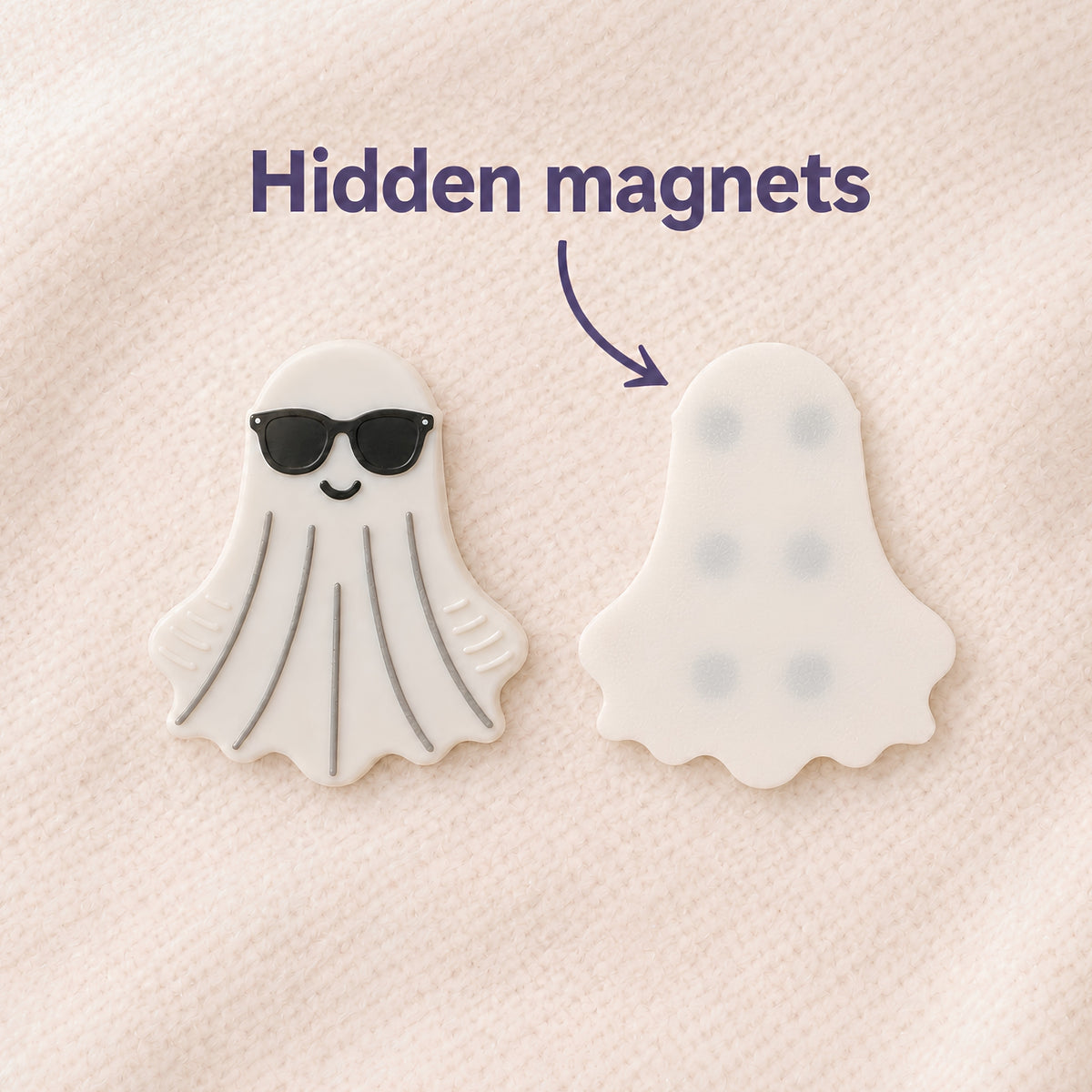 Two ghost-shaped items on a soft off-white blanket textured background, with text reading 'Hidden magnets' and an arrow pointing to the back of the ghost fidget on the right showing the magnet pattern. The front side of the fidget on the left shows black sunglasses and has gray tactile lines.