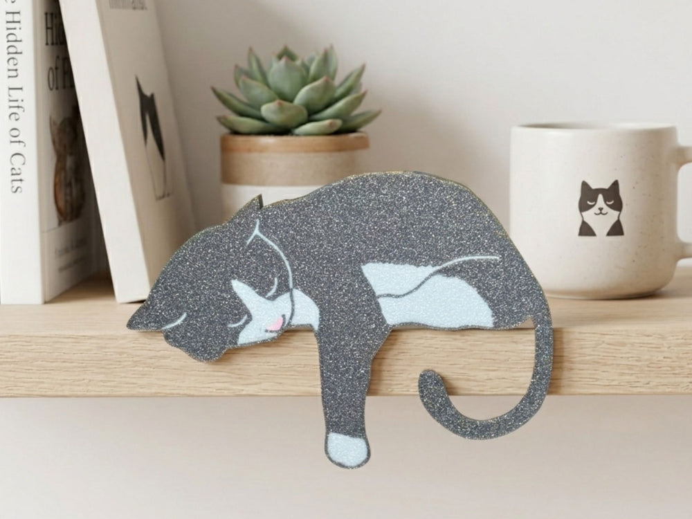 Gray and white cat-shaped decorative item on a shelf with books, a plant, and a mug.