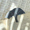 Gray cat-shaped paper clip on an open book with a textured background shimmering in the sunlight