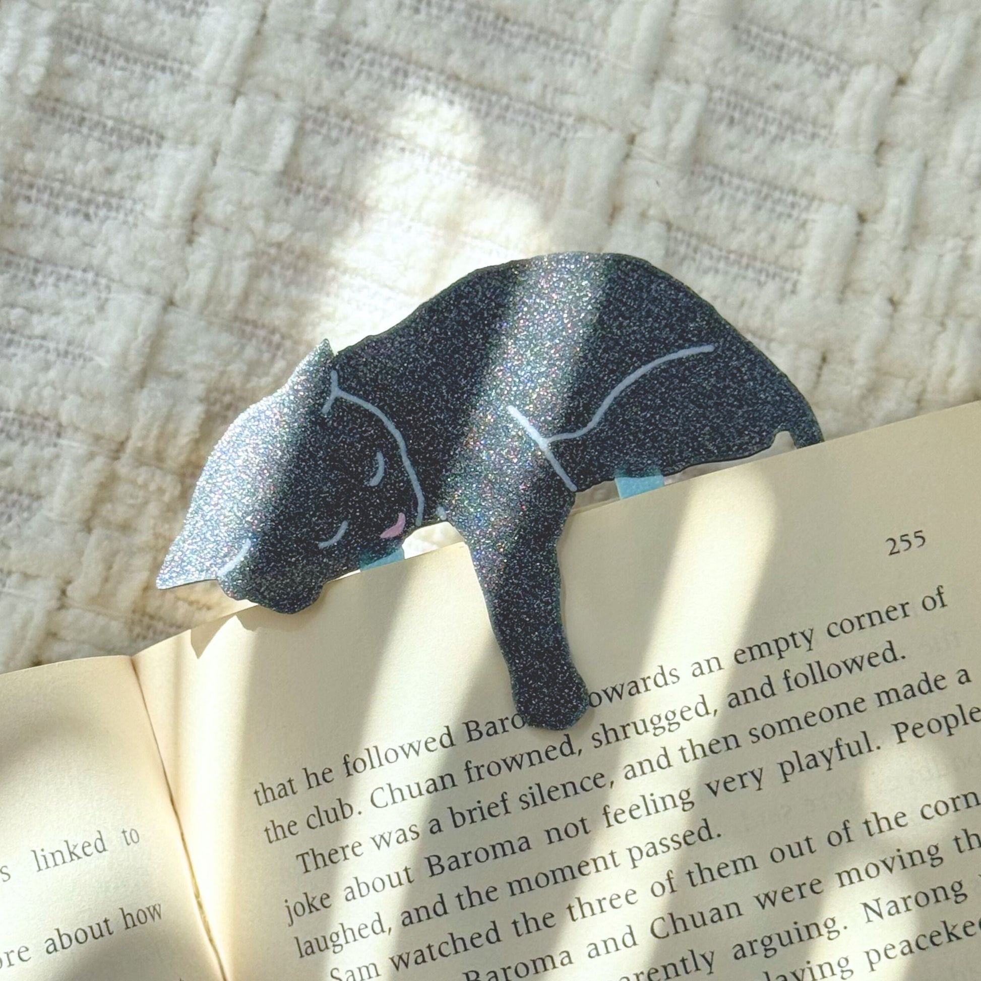 Gray cat-shaped paper clip on an open book with a textured background shimmering in the sunlight