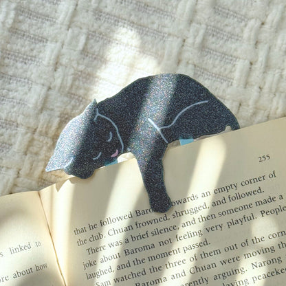 Gray cat-shaped paper clip on an open book with a textured background shimmering in the sunlight