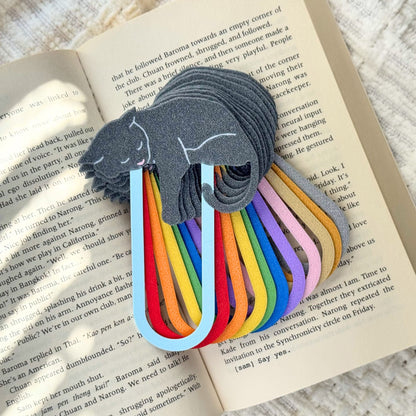 Set of rainbow-colored bookmarks with a gray cat design on an open book.