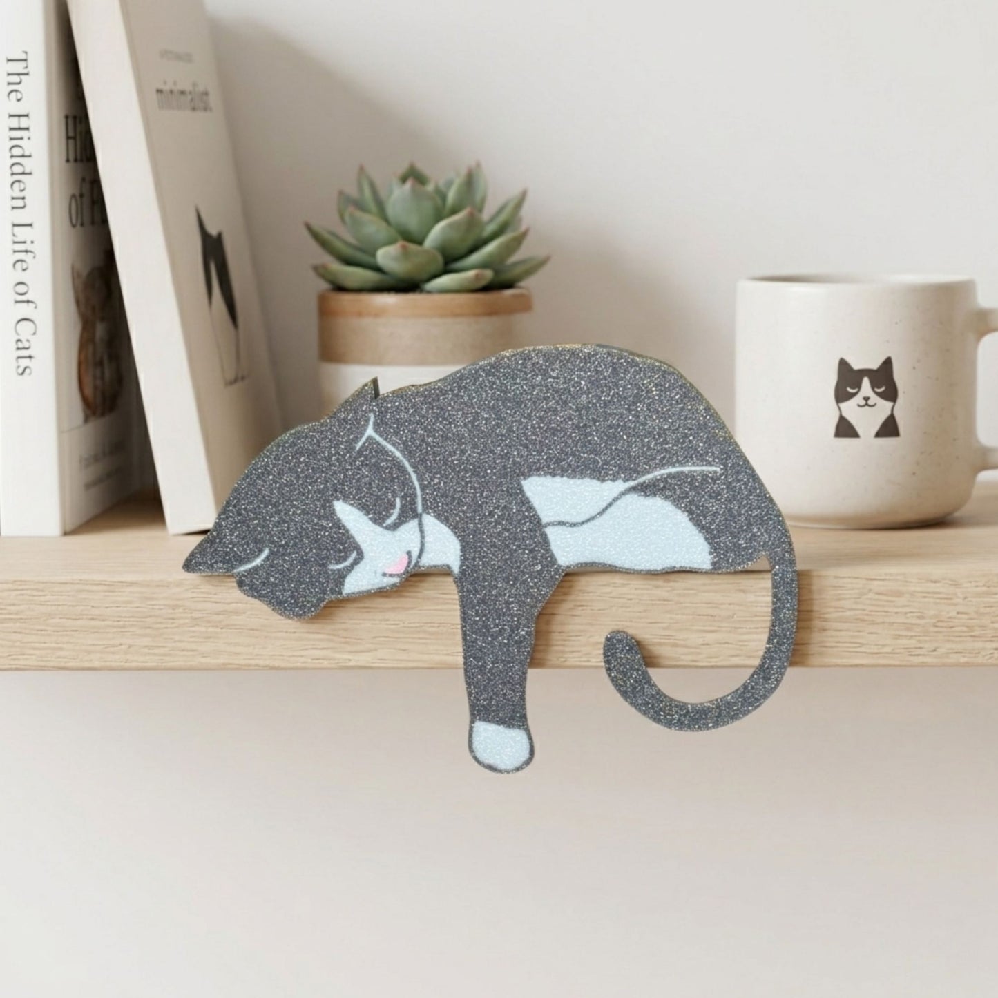 Gray and white cat-shaped decorative item on a shelf with books, a plant, and a mug in the background.