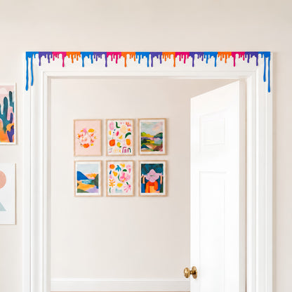 Multicolor liquid drip door topper spanning the full top trim of a white doorway with a gallery wall behind