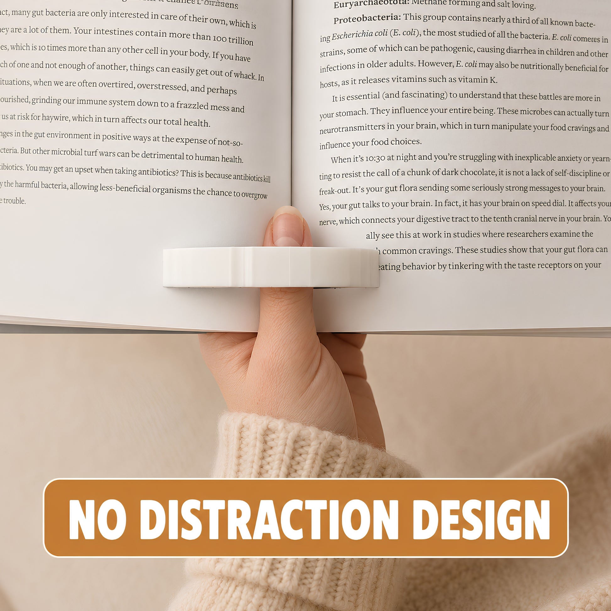 A hand holding a book open with a white cat page holder, with a bold orange banner at the bottom reading 'NO DISTRACTION DESIGN'.