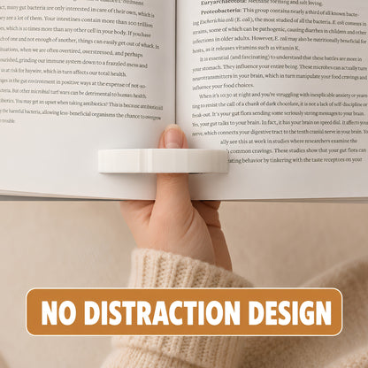 A hand holding a book open with a white cat page holder, with a bold orange banner at the bottom reading 'NO DISTRACTION DESIGN'.
