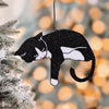 Black and white tuxedo cat ornament with pink toe beans hanging on a frosted Christmas tree branch, surrounded by warm holiday lights, perfect gift for cat parents and festive home decor