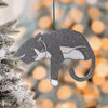 Gray and white tuxedo cat ornament with pink toe beans hanging on a frosted Christmas tree branch, surrounded by warm holiday lights, perfect gift for cat parents and festive home decor