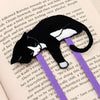 A black and white tuxedo cat-shaped bookmark with purple paperclip, resting on an open book page.