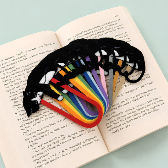 A black and white tuxedo cat-shaped bookmarks showcasing multiple color variations for the page clip, resting on an open book.