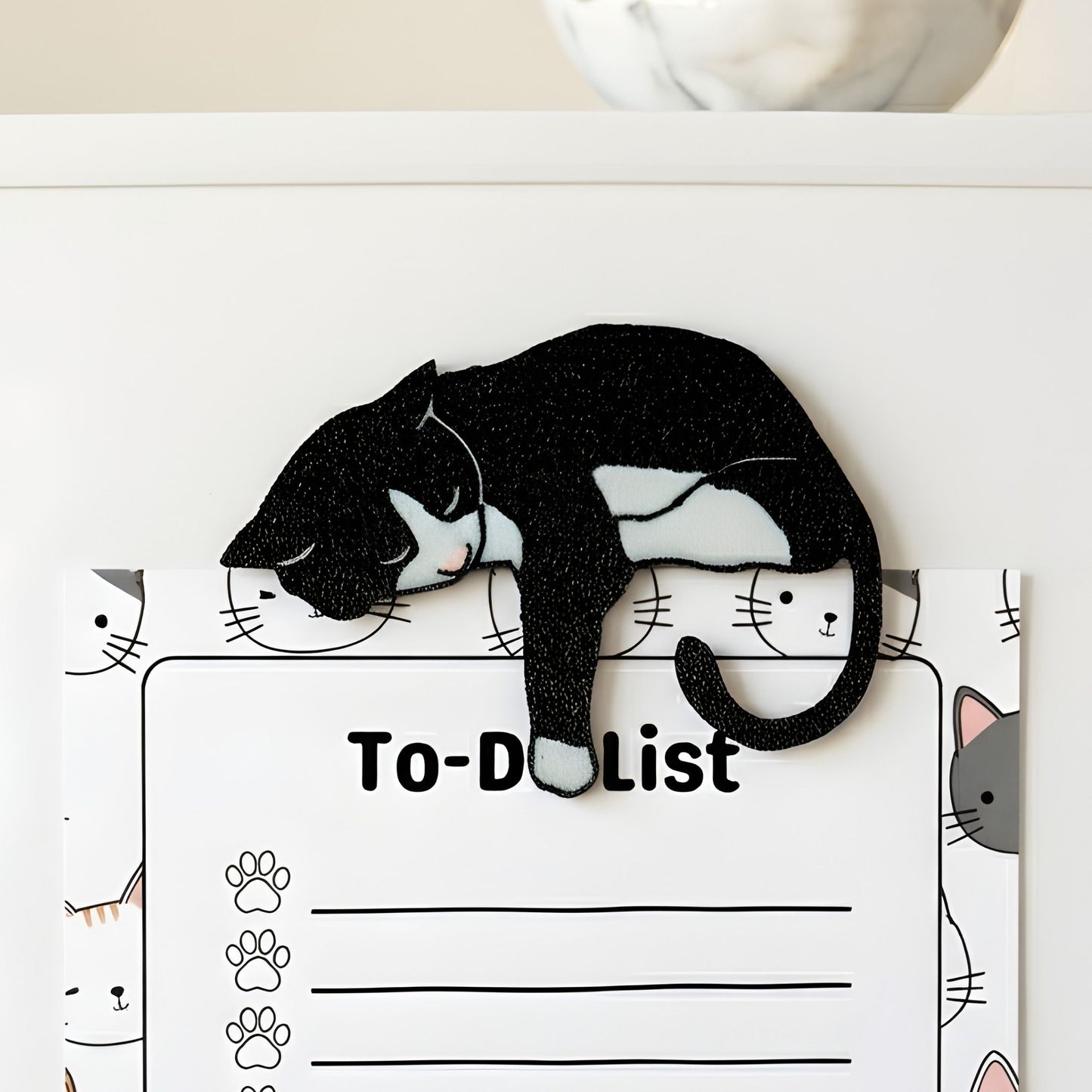 Black tuxedo cat fridge magnet holding a cat-themed to-do list on a refrigerator